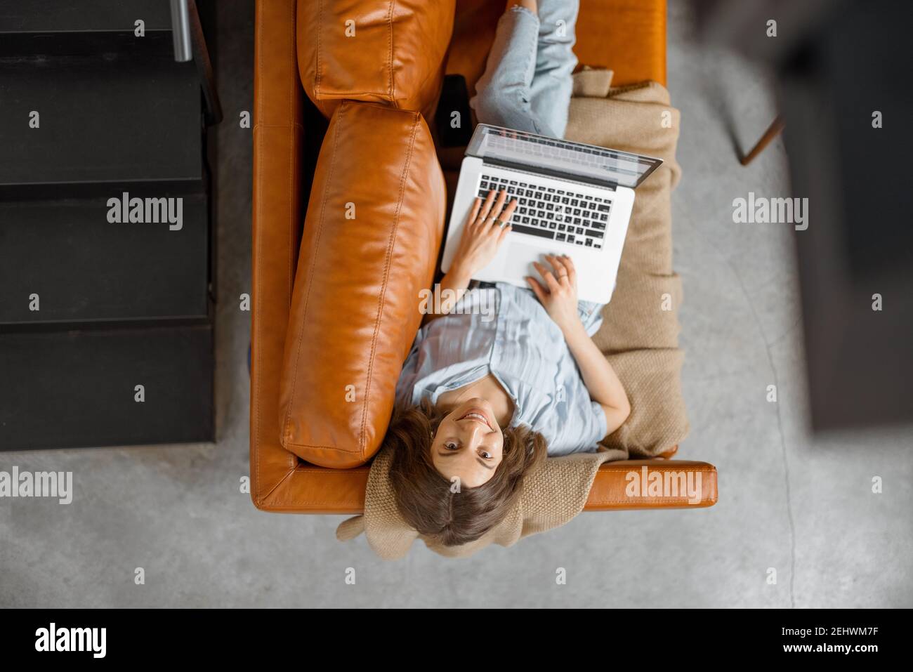 Donna che lavora con un computer portatile da casa su un divano Foto Stock