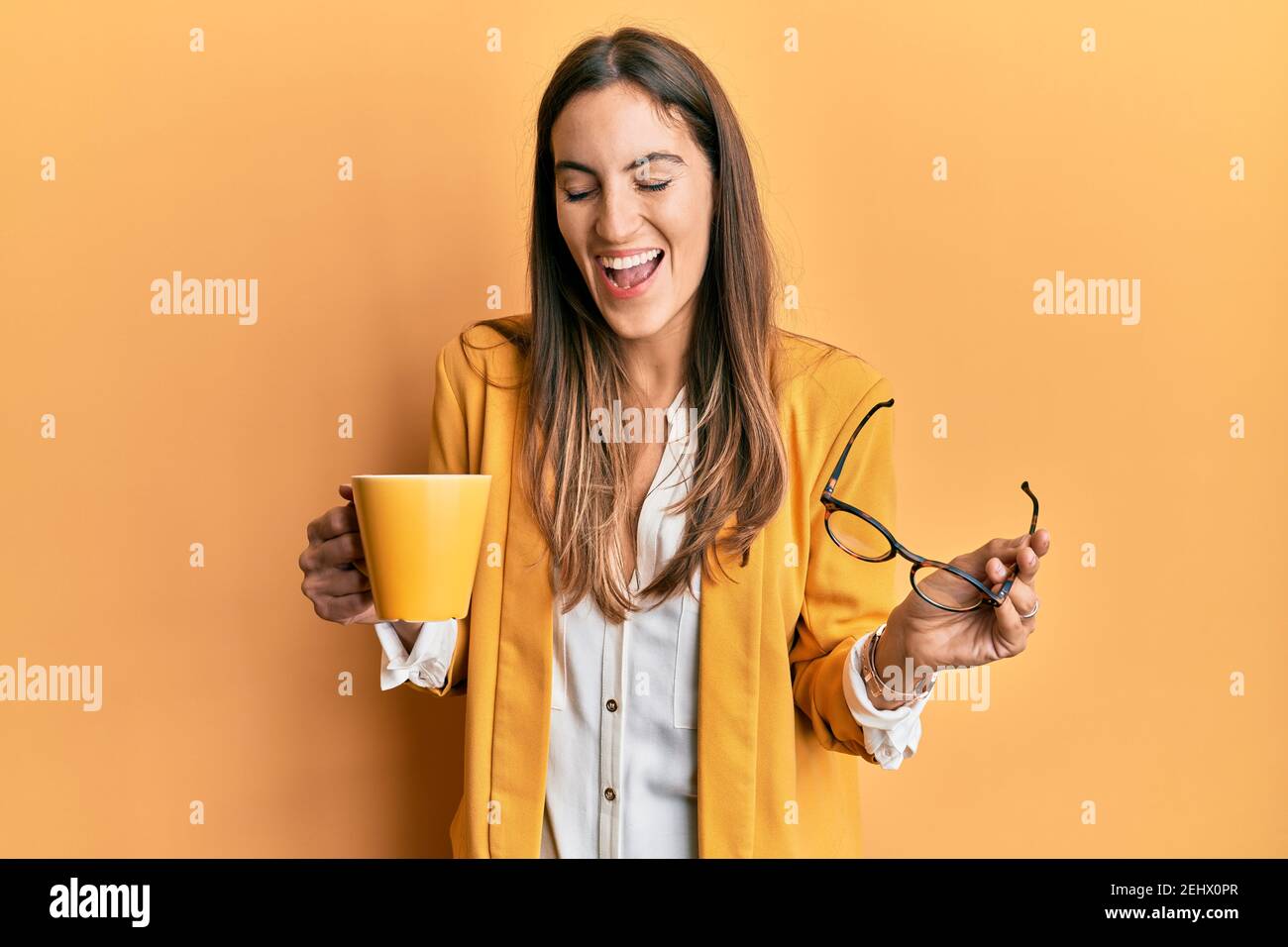 Giovane bella donna che indossa stile business bere tazza di caffè sorridente e ridendo forte fuori forte perché divertente scherzo pazzo. Foto Stock