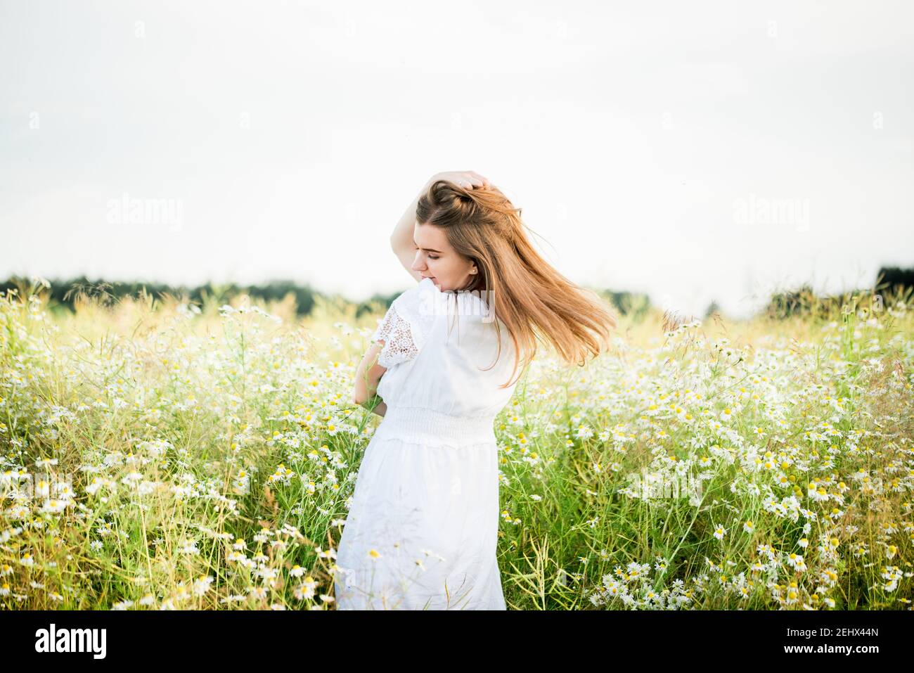 Ragazza felice sul campo camomilla, tramonto estivo. In un vestito bianco. Correre e filare, il vento nei miei capelli, stile di vita. Concetto di libertà e caldo Foto Stock