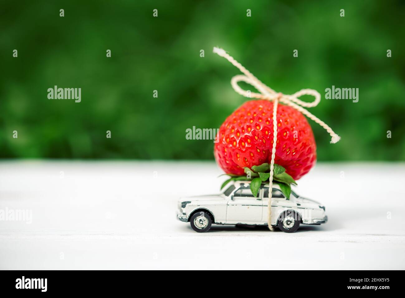 Su uno sfondo verde una piccola auto giocattolo con fragole rosse luogo iscrizione.concetto estate è in arrivo, stagioni Foto Stock