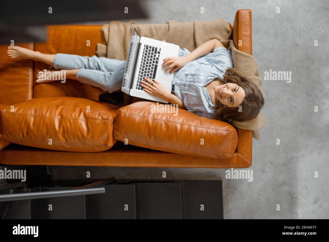 Donna che lavora con un computer portatile da casa su un divano Foto Stock