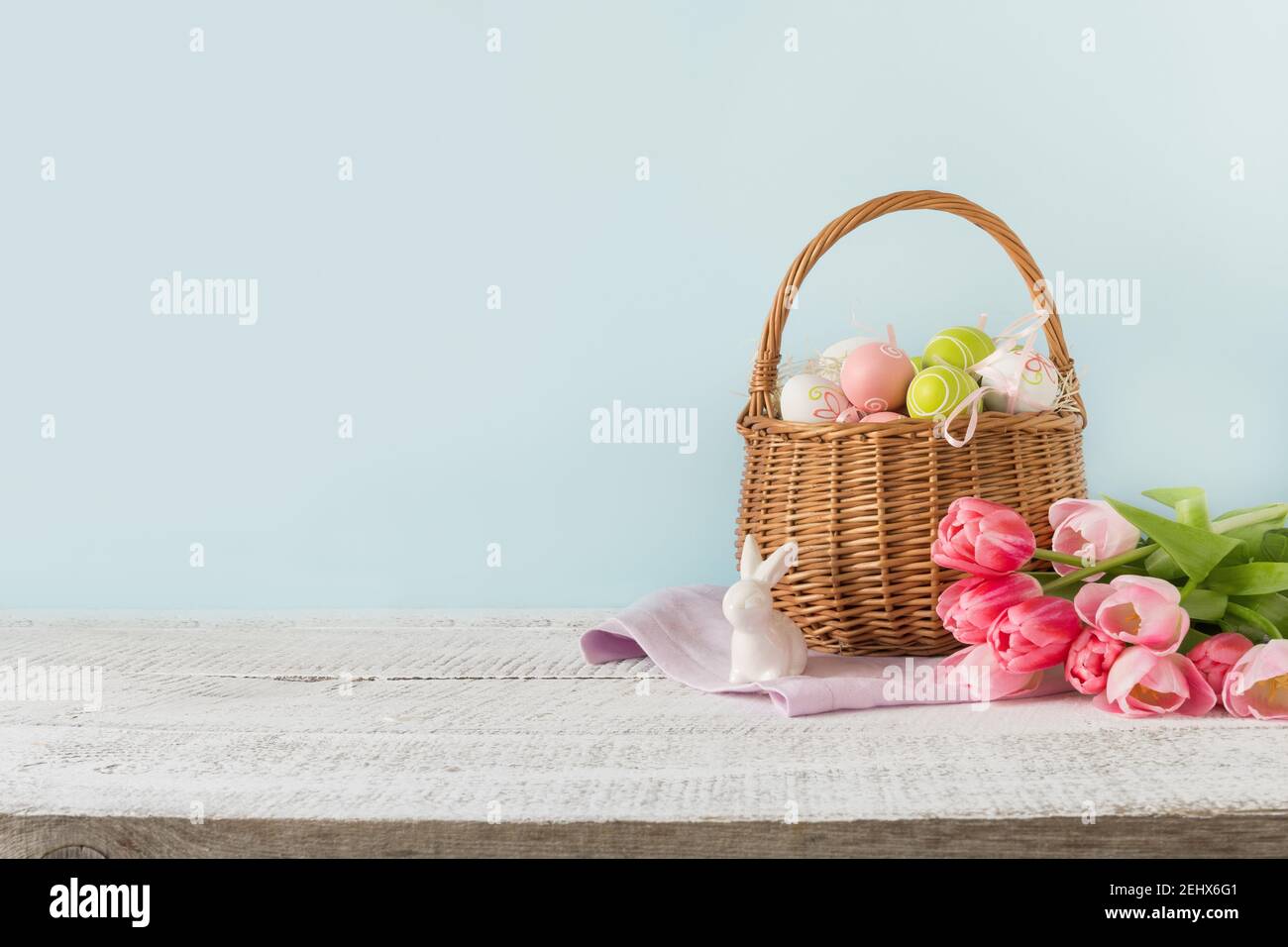 Cesto di vimini pasquali con uova dipinte e tulipani rosa su sfondo blu con spazio per il testo. Foto Stock