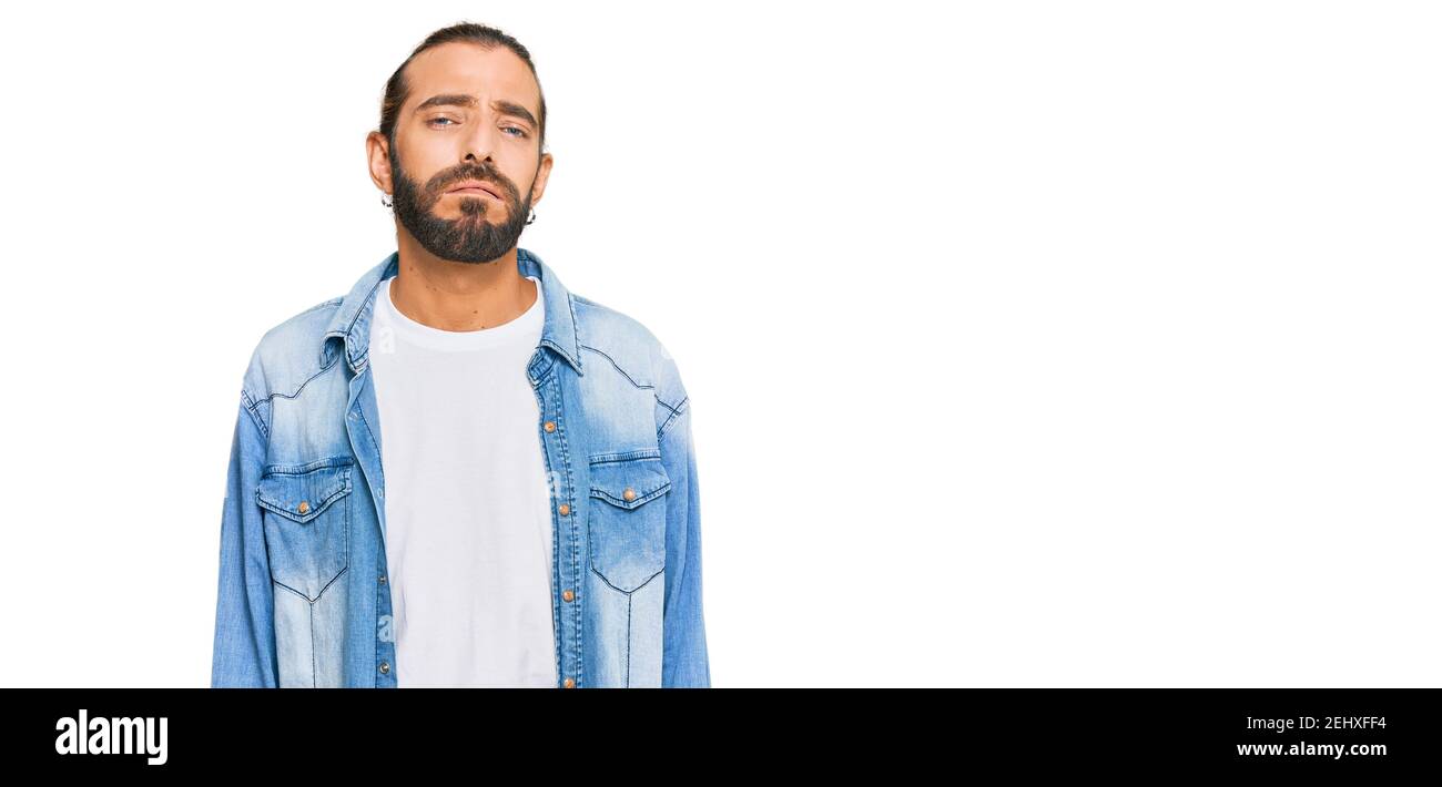 Uomo attraente con capelli lunghi e barba che indossa giacca casual in denim che guarda sonnolento e stanco, esausto per fatica e sbornia, occhi pigri nella mor Foto Stock