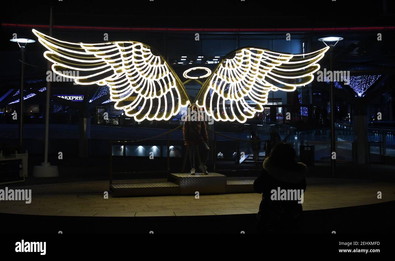 Una giovane ragazza si pone di fronte ad un paio di ali d'angelo illuminate a Chavasse Park, Liverpool, Inghilterra Foto Stock