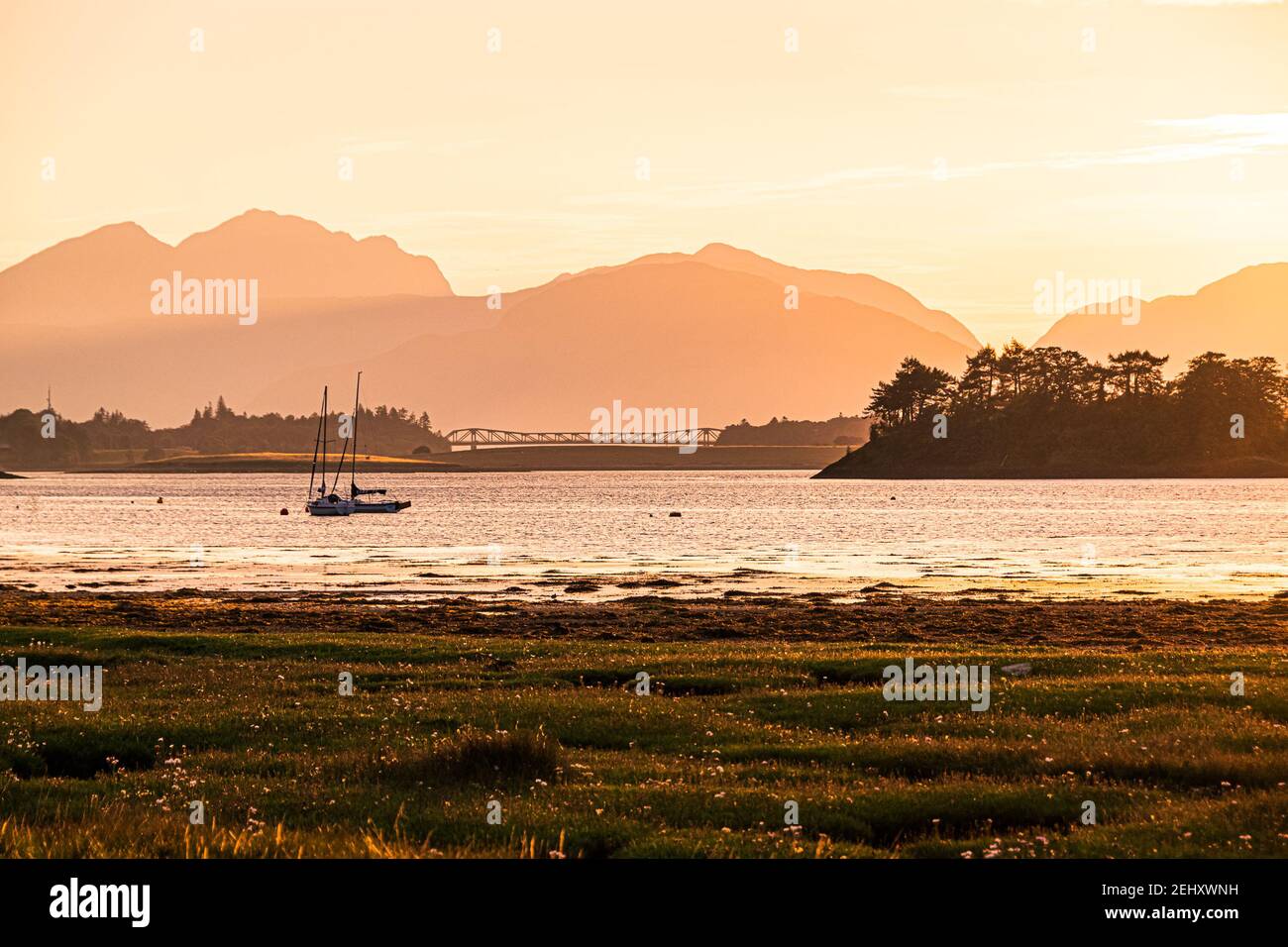 Tramonto su Loch Leven, Glencoe, Scozia. Tramonto colorato sul Loch Leven con una barca ormeggiata e una silhouette del Fort William Bridge all'orizzonte. Foto Stock