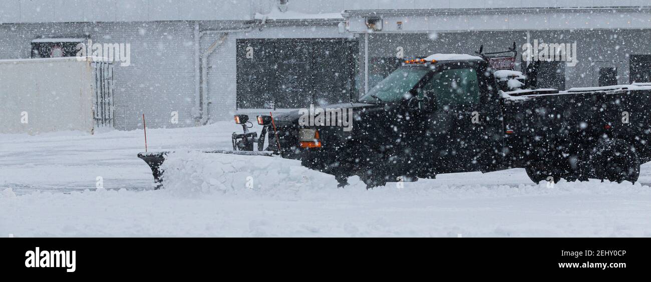 Un camion nero di proprietà di un appaltatore privato sta arando la neve nel parcheggio di un'azienda durante una tempesta di neve. Foto Stock