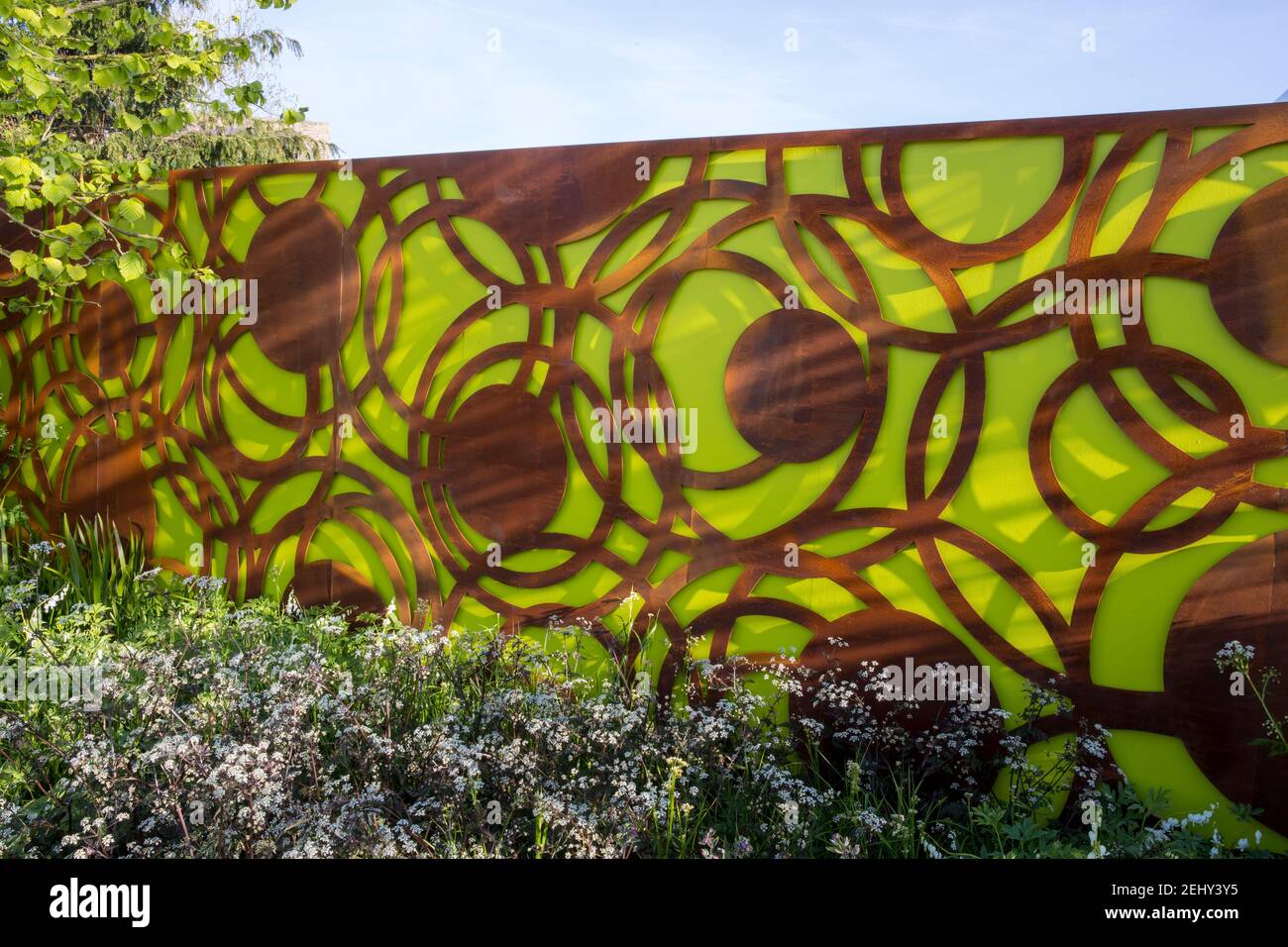 Un moderno e contemporaneo giardino urbano recinzione pannelli con corten acciaio E colore verde - cielo blu in primavera Inghilterra GB Confini fioriti del Regno Unito Foto Stock