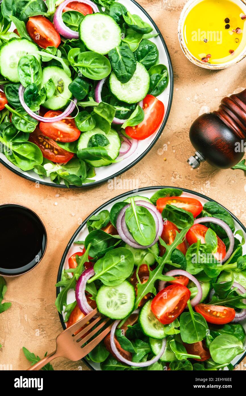 Insalata verde primaverile con spinaci, pomodori ciliegini, insalata di mais e cipolla rossa. Concetto di cibo sano. Tavolo in pietra beige. Vista dall'alto. Spazio di copia Foto Stock