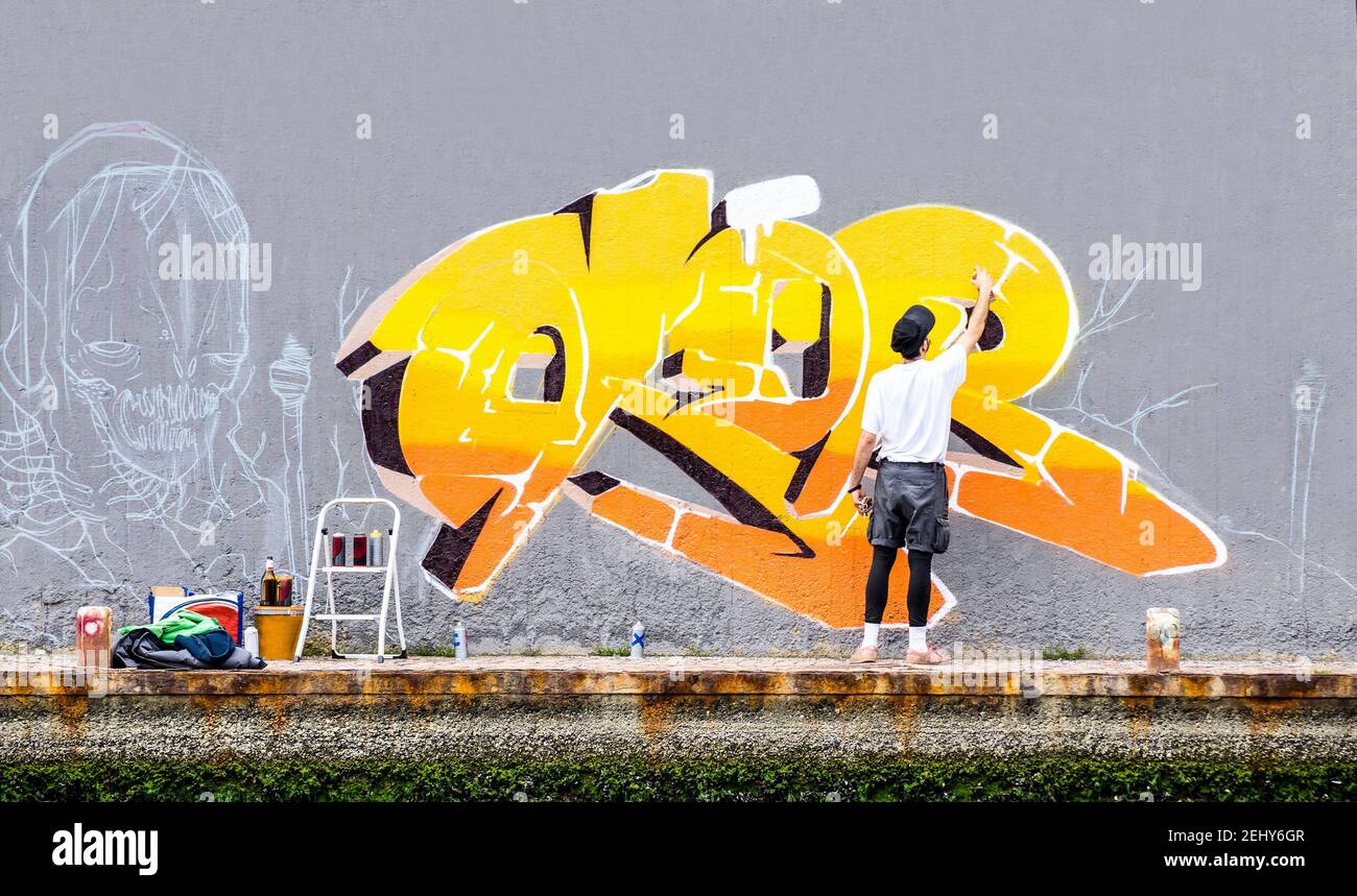 Artista di strada pittura graffiti colorati sulla parete dello spazio pubblico - Concetto di arte moderna di un ragazzo urbano che si esibisce e si prepara dal vivo pitture murali Foto Stock