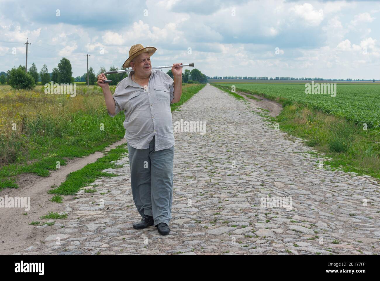 Ritratto esterno dell'agricoltore ucraino anziano in piedi cappello di paglia su strada acciottolata e prendendo bastone a piedi Foto Stock