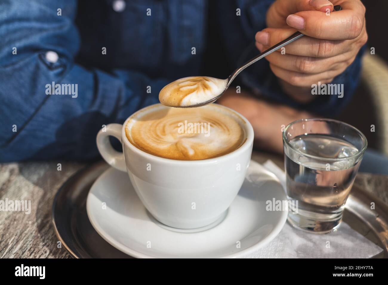 Cappuccino, donna che beve caffè al bar. Vista ravvicinata del cucchiaio in mano femminile e tazza di caffè bianca Foto Stock