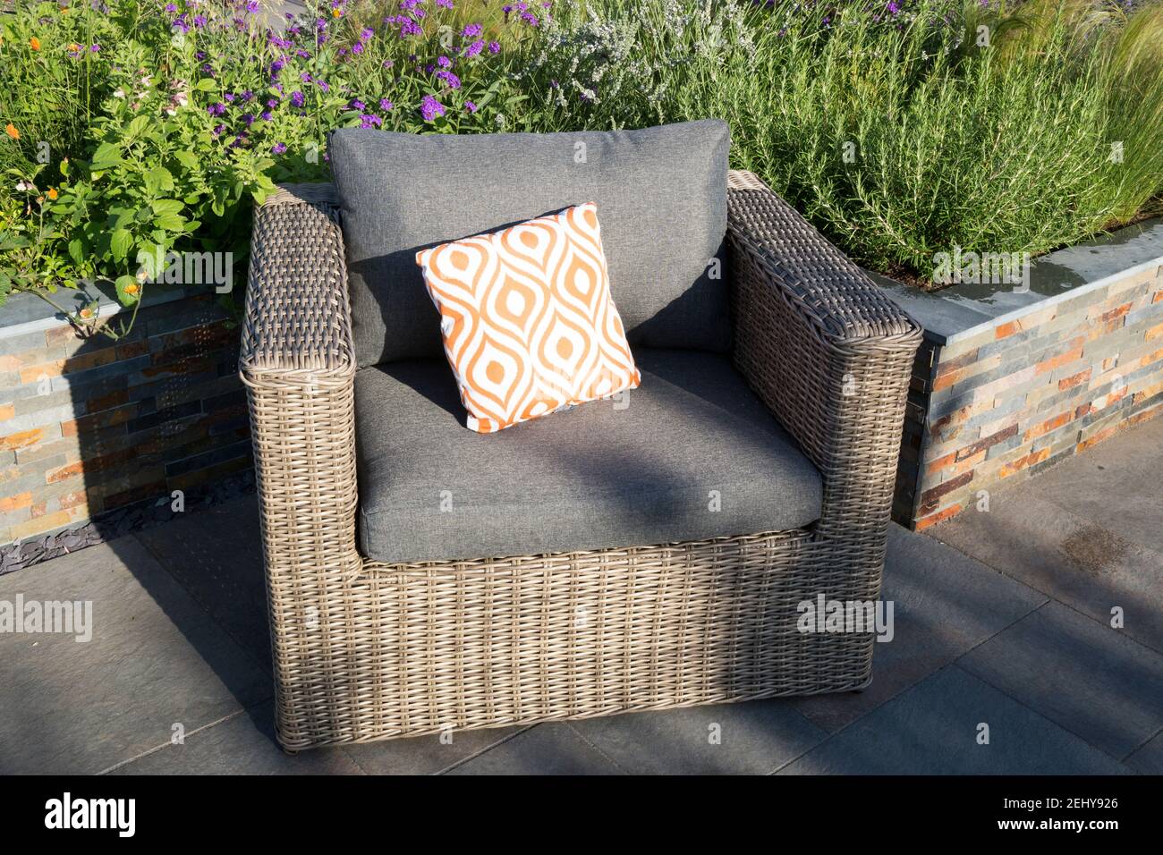 Patio esterno dal design moderno del giardino con mobili da pranzo in rattan acrilico con tavolo e sedie, cuscino arancione, letti rialzati in ardesia di rame lucente GB Foto Stock