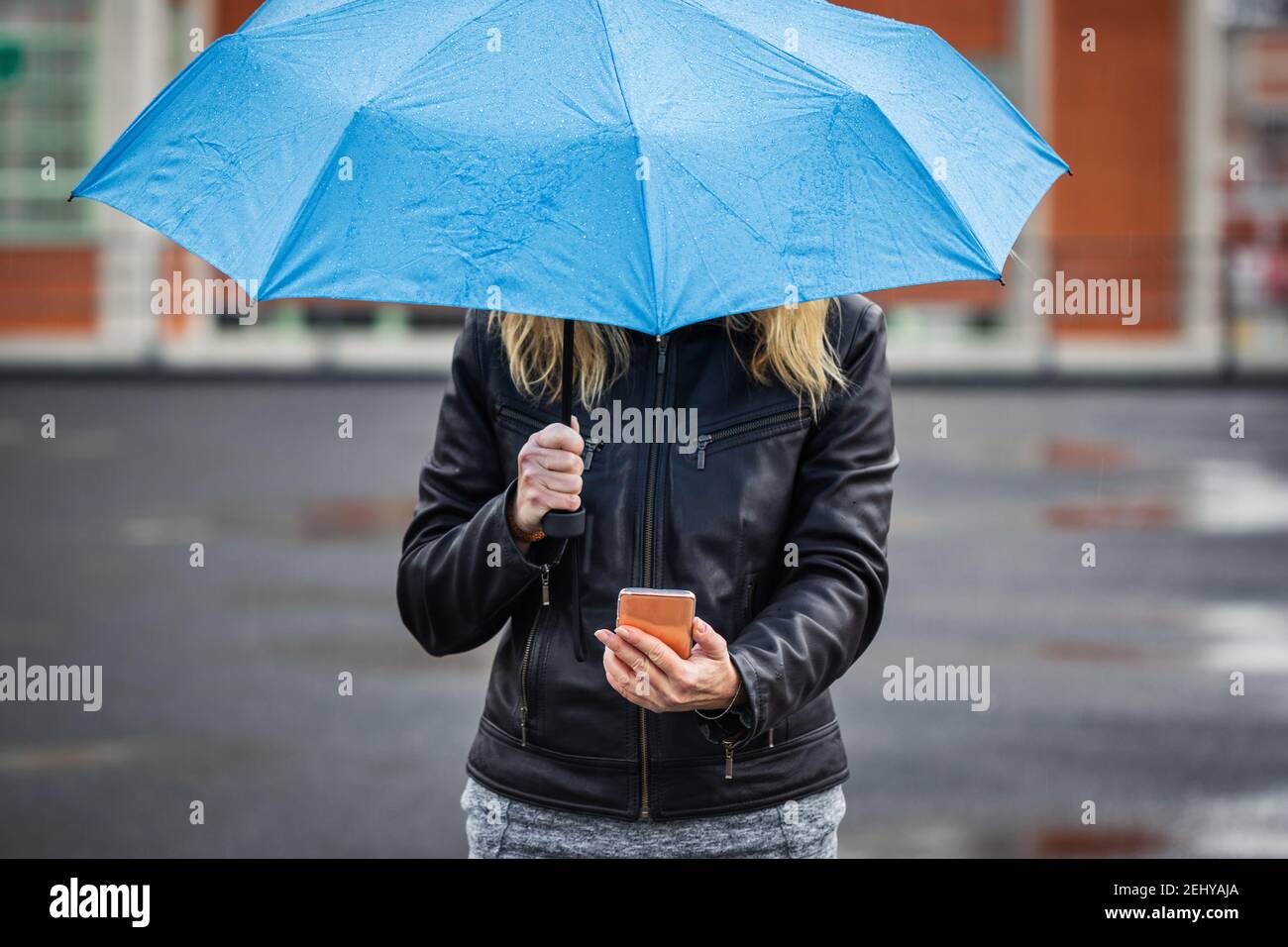 Donna con ombrello che tiene smartphone e in piedi sotto la pioggia in strada. Connessione internet wireless sul telefono cellulare in città Foto Stock