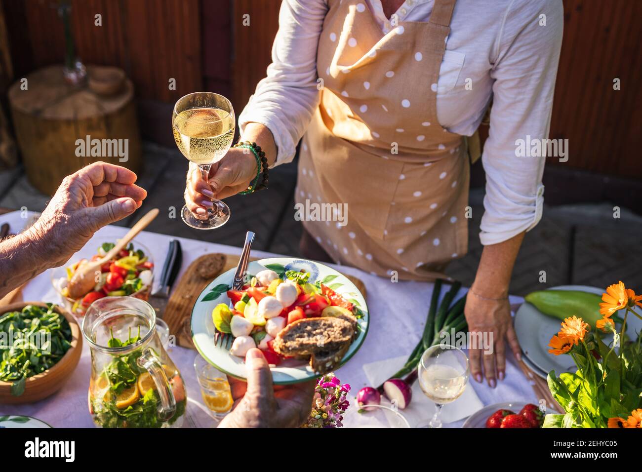 Goditi il vino bianco e l'insalata di verdure durante la festa in giardino. La donna serve cibo e bevande a un'altra persona durante un evento di celebrazione all'aperto Foto Stock