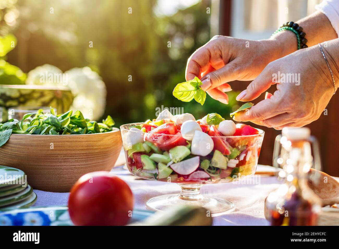 Insalata di verdure fresche finendo a mano con foglie di basilico alle erbe. Preparare cibo sano in giardino all'aperto Foto Stock