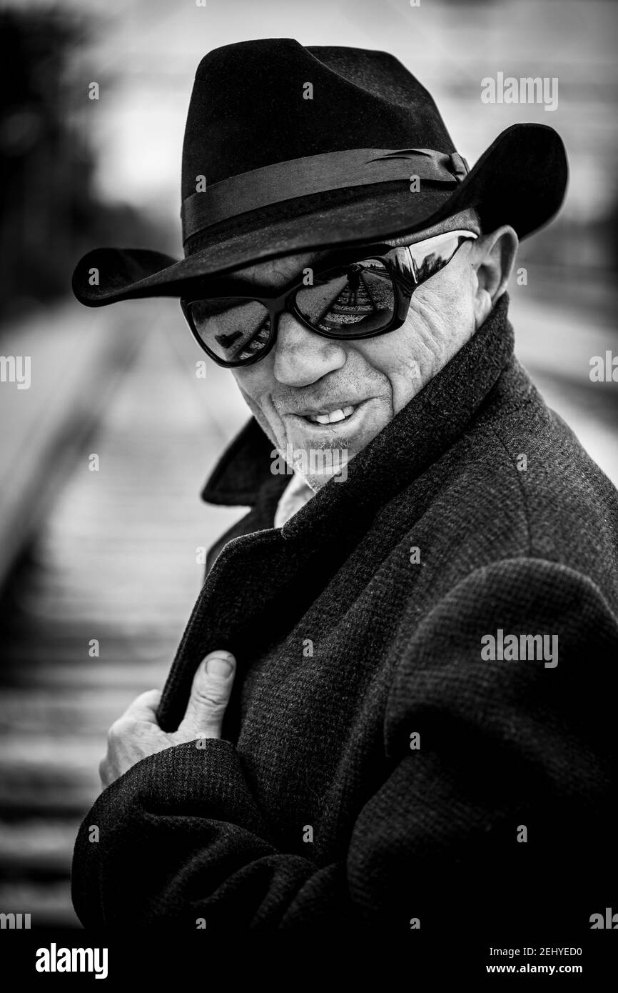 un uomo in un cappotto nero con un cappello nero e occhiali da sole neri Foto Stock