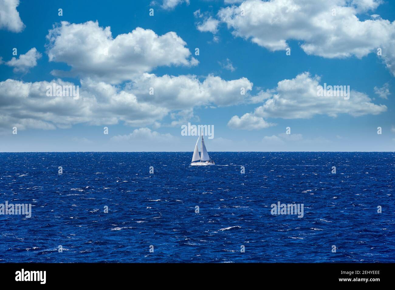 Una fotografia minimalistica di un Sailbout vela attraverso il blu profondo Mare ondulato con cielo blu e nuvole bianche nel Sfondo Foto Stock