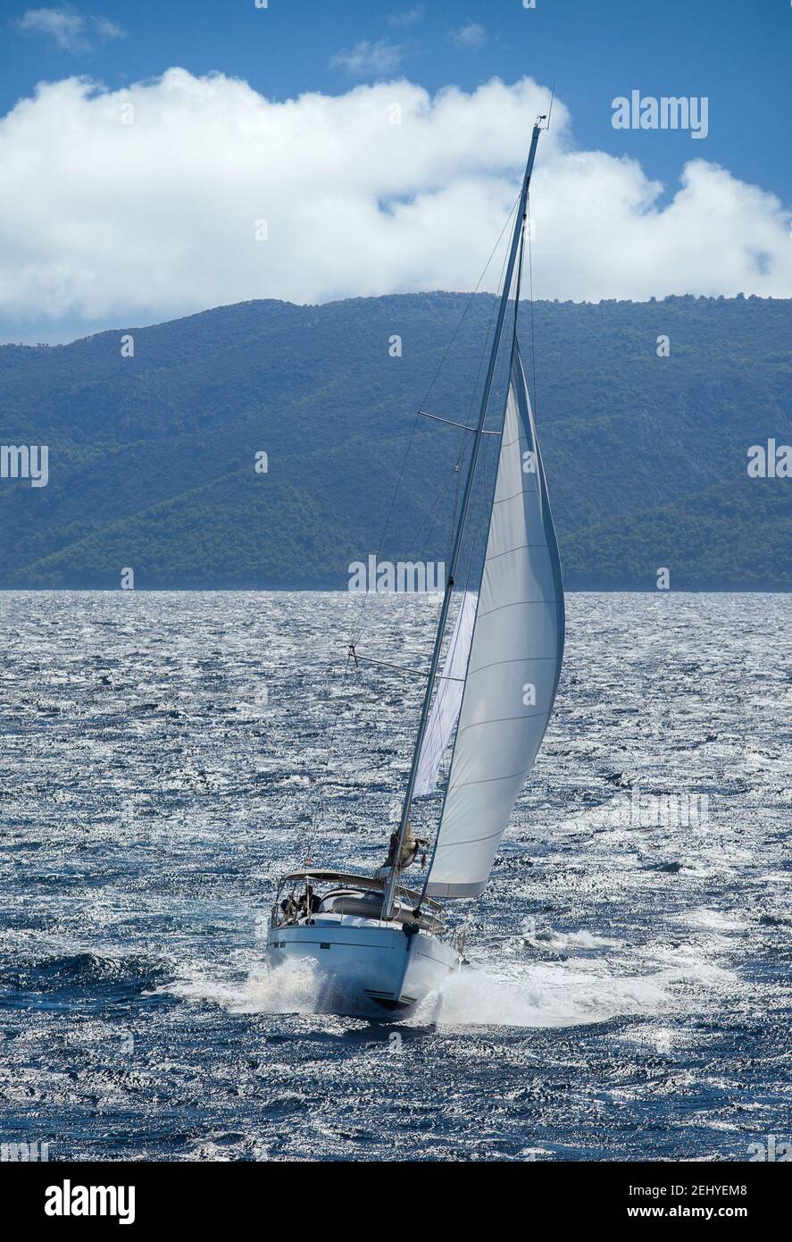 Una barca a vela che accelera attraverso un mare ondulato con una foresta Isola di Hvar in background Foto Stock