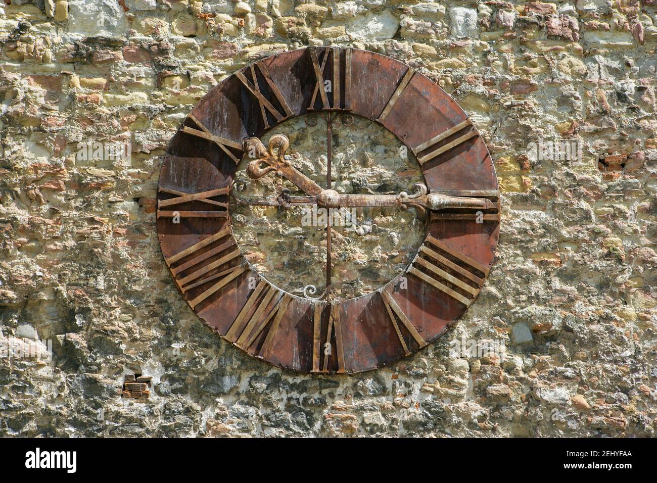 Un orologio di metallo antico con numeri romani su una pietra Parete Foto Stock