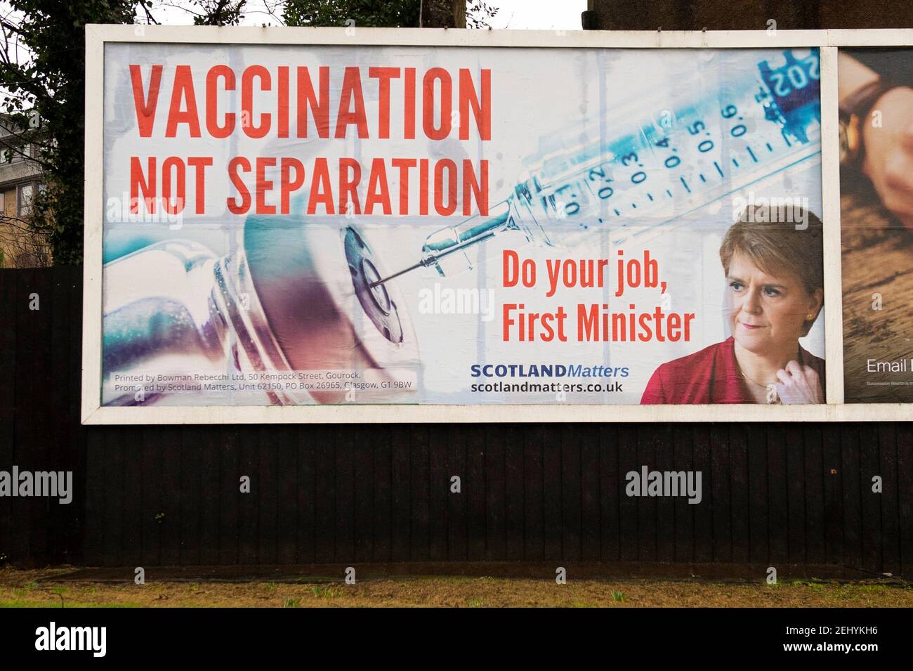 Greenock, Scozia, Regno Unito. 20 febbraio 2021. Nella foto: Immagine del primo ministro scozzese Nicola Sturgeon con la grafica di un vaccino COVID19 e una siringa con lo slogan: "VACCINAZIONE NON SEPARAZIONE. FAI IL TUO LAVORO, PRIMO MINISTRO." su un cartellone nel mezzo di Greenock, in un crocevia trafficato di Brougham St & Campbell St. Questo è in riferimento alla maggioranza silenziosa di persone in Scozia che si oppongono alla SNP cercando un secondo referendum sull'indipendenza nel mezzo di una pandemia che lo ha fatto Nel Regno Unito sono state uccise oltre 106,000 persone, di cui 6,816 nella sola Scozia. Credit: Colin Fisher/Alamy Live News. Foto Stock
