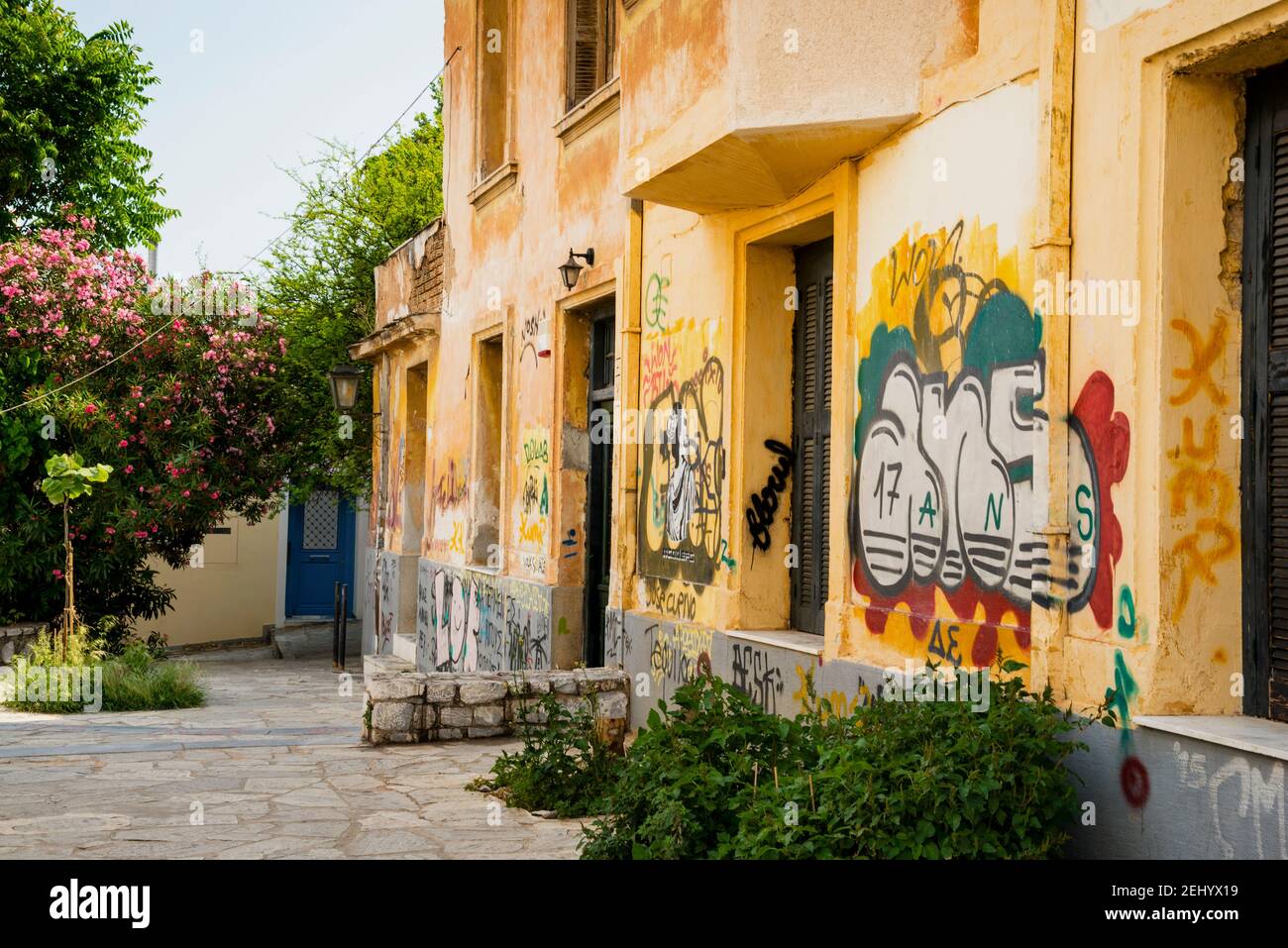 Un tranquillo cortile in pietra in contrasto con le mura coperte di graffiti di Atene, Grecia. Foto Stock