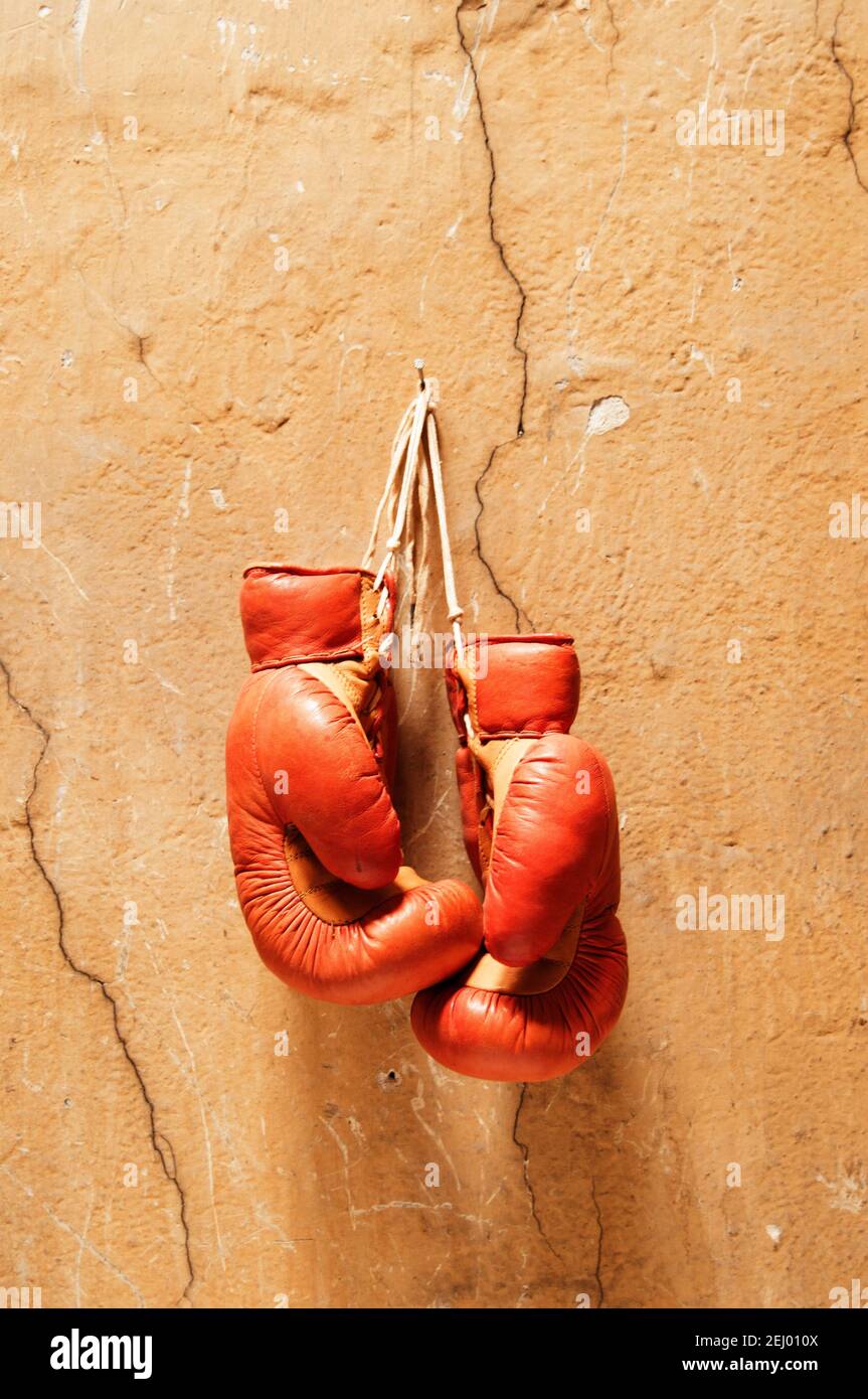 Vecchi guanti da boxe appesi su una parete incrinata, che mostrano un senso di nostalgia e lo spirito di questo sport Foto Stock