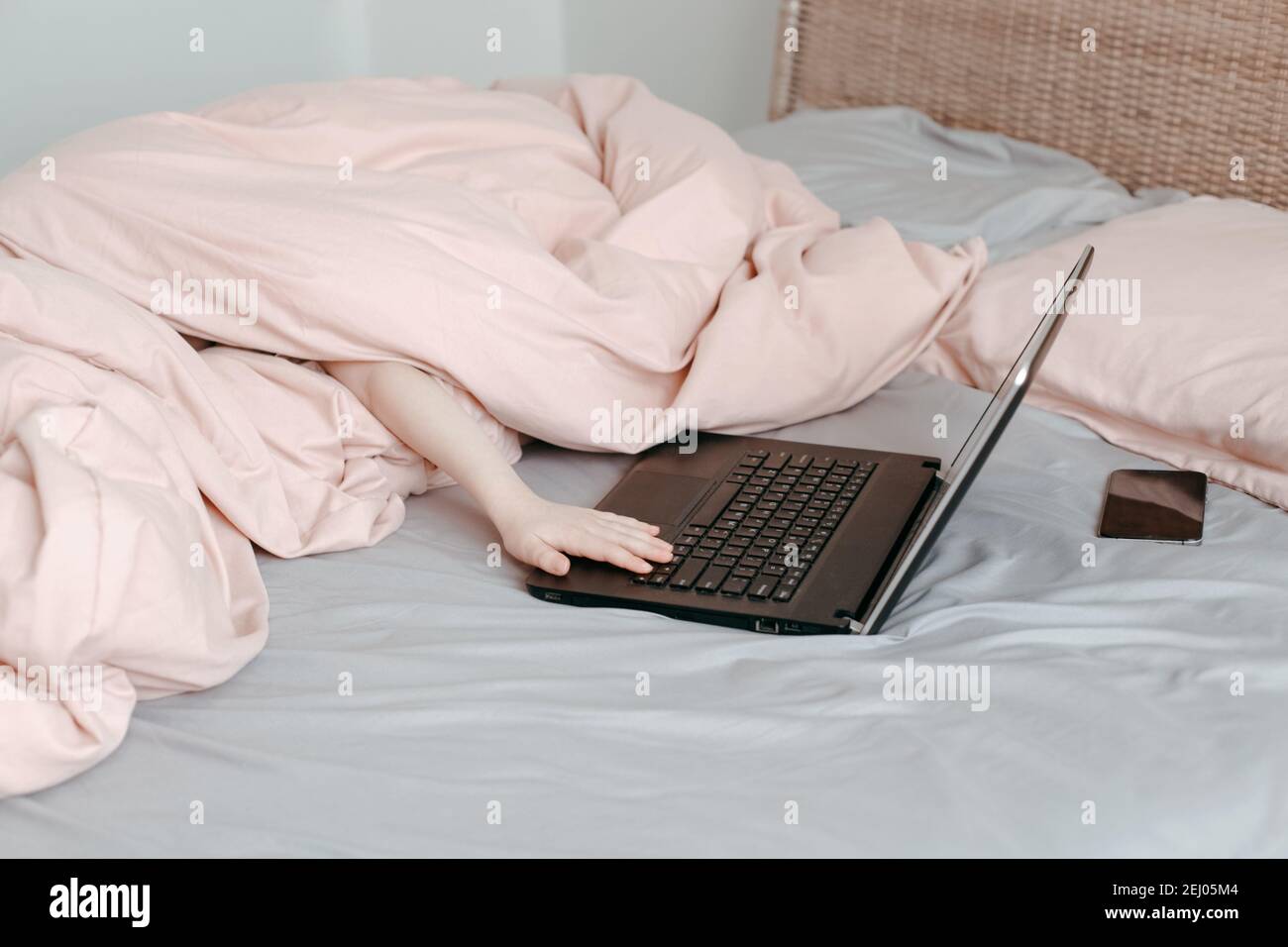Noia bambino divertente che si trova a letto sotto la coperta e l'apprendimento in classe di scuola online virtuale. Digitazione manuale sulla tastiera del computer. Bambino che lavora su un computer portatile Foto Stock