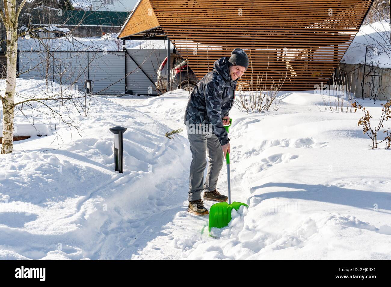 Un operaio pulisce la neve dai sentieri del giardino con una pala in una giornata di sole. Manutenzione del giardino in inverno. Grandi nevicate dopo una bizzarda. Il cortile era Foto Stock