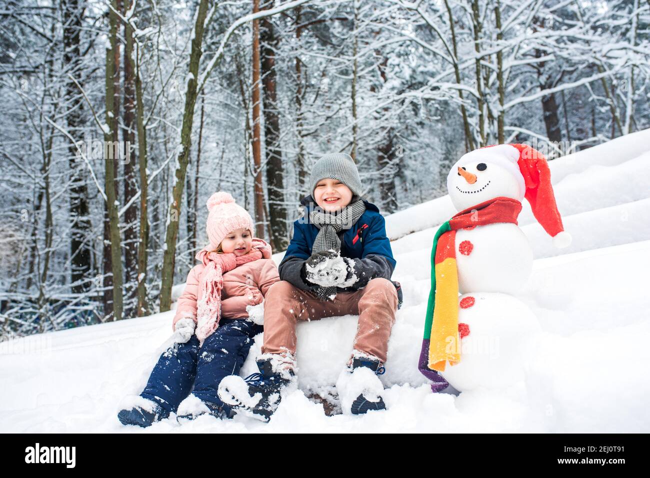 Carino ragazzo e ragazza costruire pupazzo di neve nella foresta invernale Foto Stock