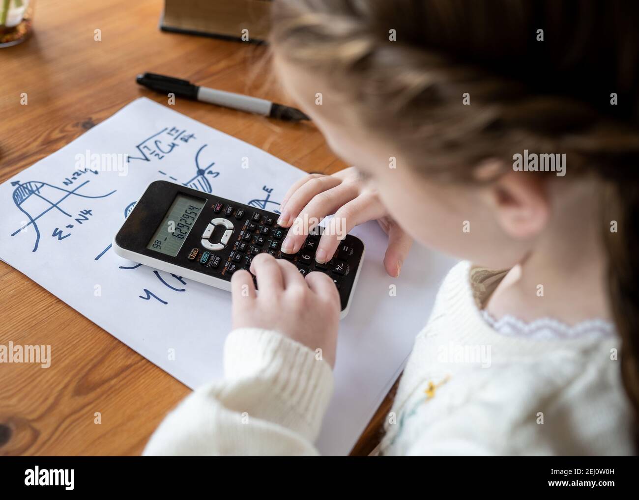 Carino giovane ragazza carina facendo calcoli complessi di scrittura matematica genio bambino a casa scuola utilizzando la calcolatrice scientifica per fare avanzate aritmetica Foto Stock