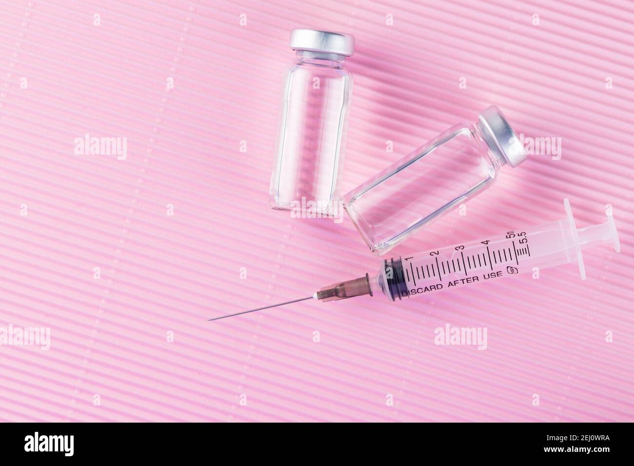 Concetto di cura sanitaria con iniezione di vaccino e siringa. Vaccini e siringhe su sfondo rosa per la prevenzione e l'immunizzazione. Spazio di copia. In alto Foto Stock