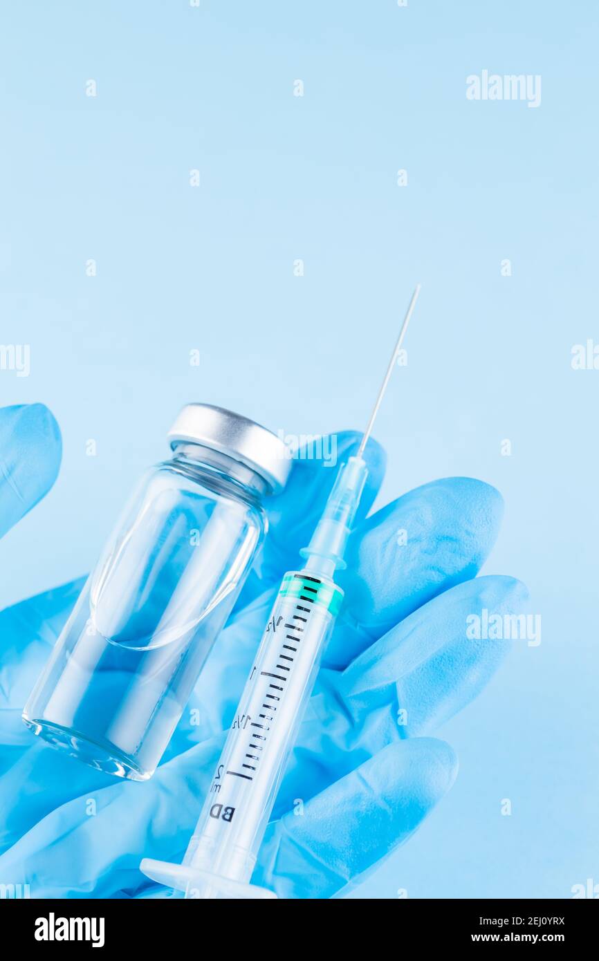 Flaconcino di vaccino e siringa in mano del medico. La mano del medico nel guanto chirurgico che tiene un flaconcino di vaccino e una siringa. Vaccinazione e immunizzazione Foto Stock