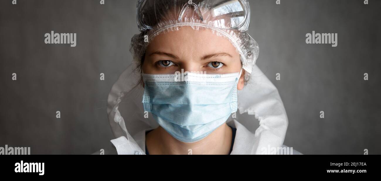 Donna che indossa occhiali protettivi e maschera medica viso a causa di COVID-19 coronavirus pandemia, banner panoramico con ritratto di dottore o infermiera femminile Foto Stock