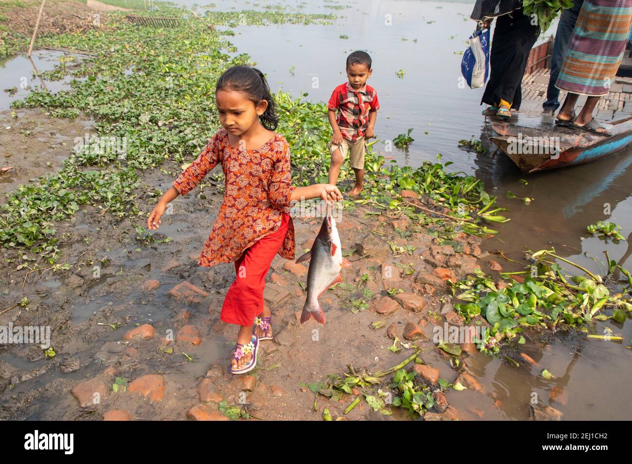 Una ragazza tiene un pesce sulla riva del fiume Titas a Brahmanbaria, Bangladesh Foto Stock