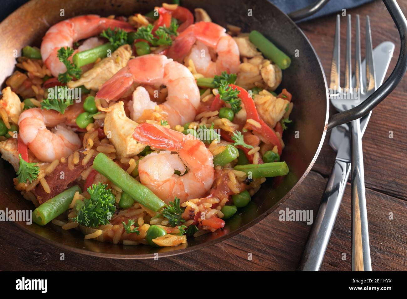 Piatto di pesce con gamberi, riso, carne di pollo e verdure in paella su un tavolo di legno rustico scuro, fuoco selezionato Foto Stock