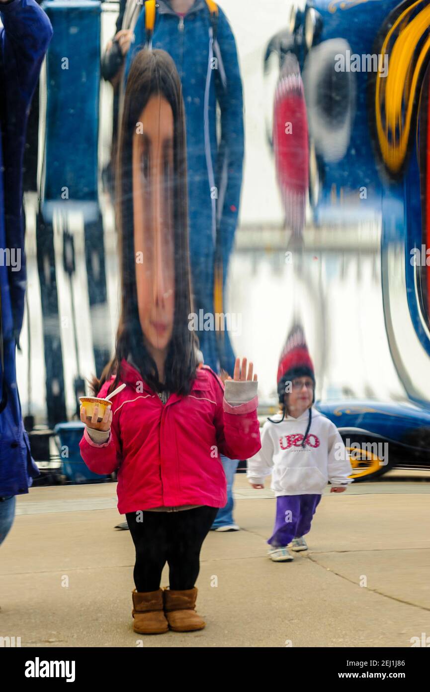 Specchio funhouse, l'immagine di una giovane ragazza che indossa una giacca rossa si riflette sulla superficie di uno specchio distorsivo a Navy Pier, Chicago, Illinois. Foto Stock