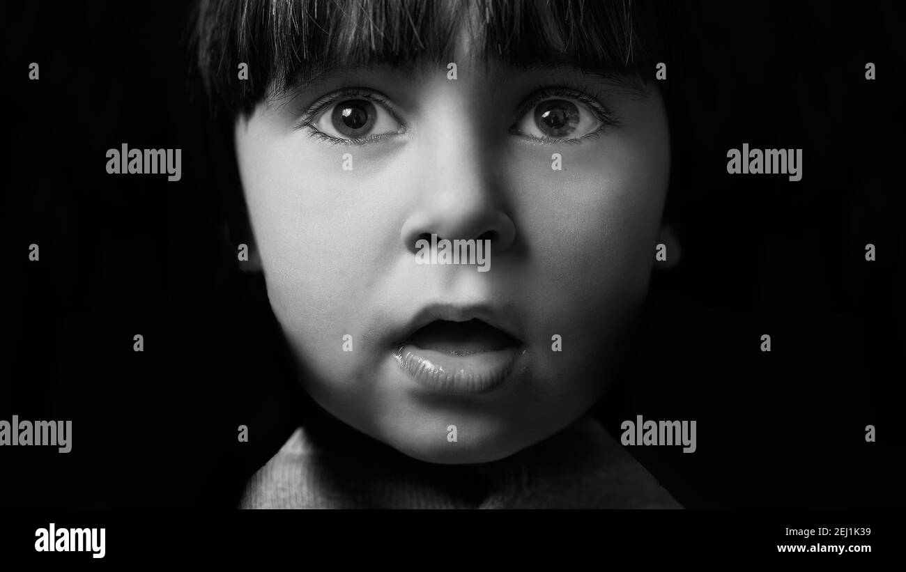 ragazzo di 3 anni che guarda curiosamente alla macchina fotografica. ritratto monocromatico su fondo nero pieno. espressione di stupore, sorpresa o atonicismo. clo Foto Stock