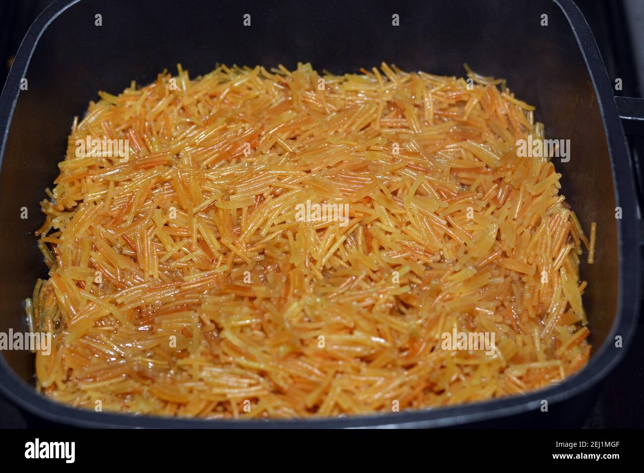 Rosolato in vermicelli egiziani dolci al burro cotti con acqua e zucchero in un recipiente da cucina, tradizionale dessert egiziano a pranzo e cena presto Foto Stock