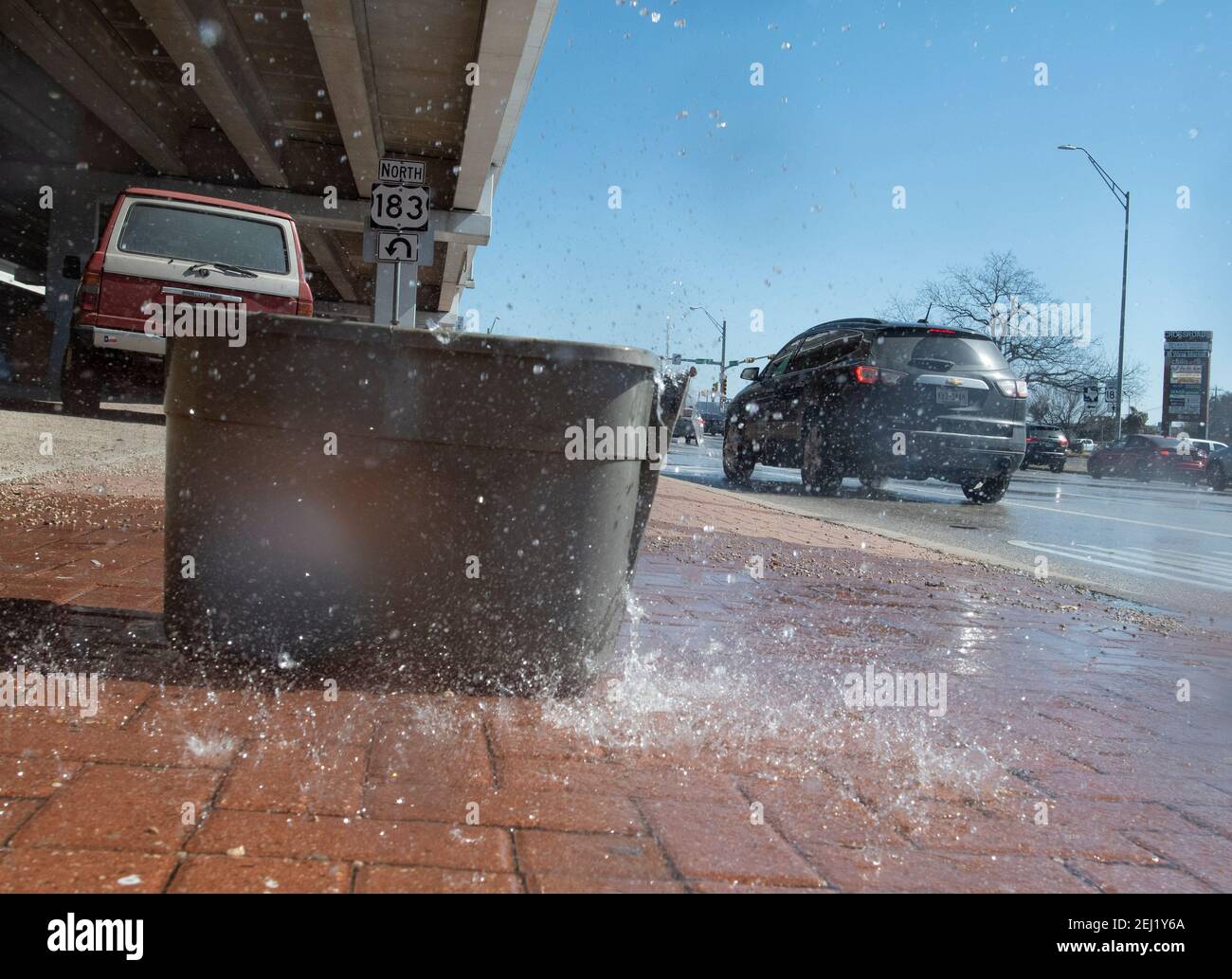 Austin, Texas USA 20 febbraio 2021: Un grande bidone di plastica è posto per catturare l'acqua dalla neve di fusione che gocciola da una sezione elevata della US Highway 183 nel nord di Austin al luogo di un accampamento senza tetto che tiene quasi una dozzina di persone. Molti residenti sono scappati per riscaldare rifugi durante il record freddo e nevicate, ma ha iniziato a tornare al campo come le temperature sono salite durante il fine settimana. Credit: Bob Daemmrich/Alamy Live News Foto Stock