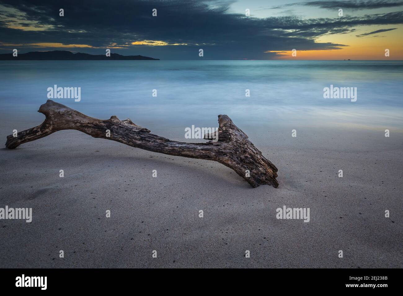 Lunga esposizione tropicale estate calmo tramonto paesaggio in spiaggia con sabbia, acqua blu setosa, tronco, mare liscio, cielo con nuvole, Costa Rica Foto Stock