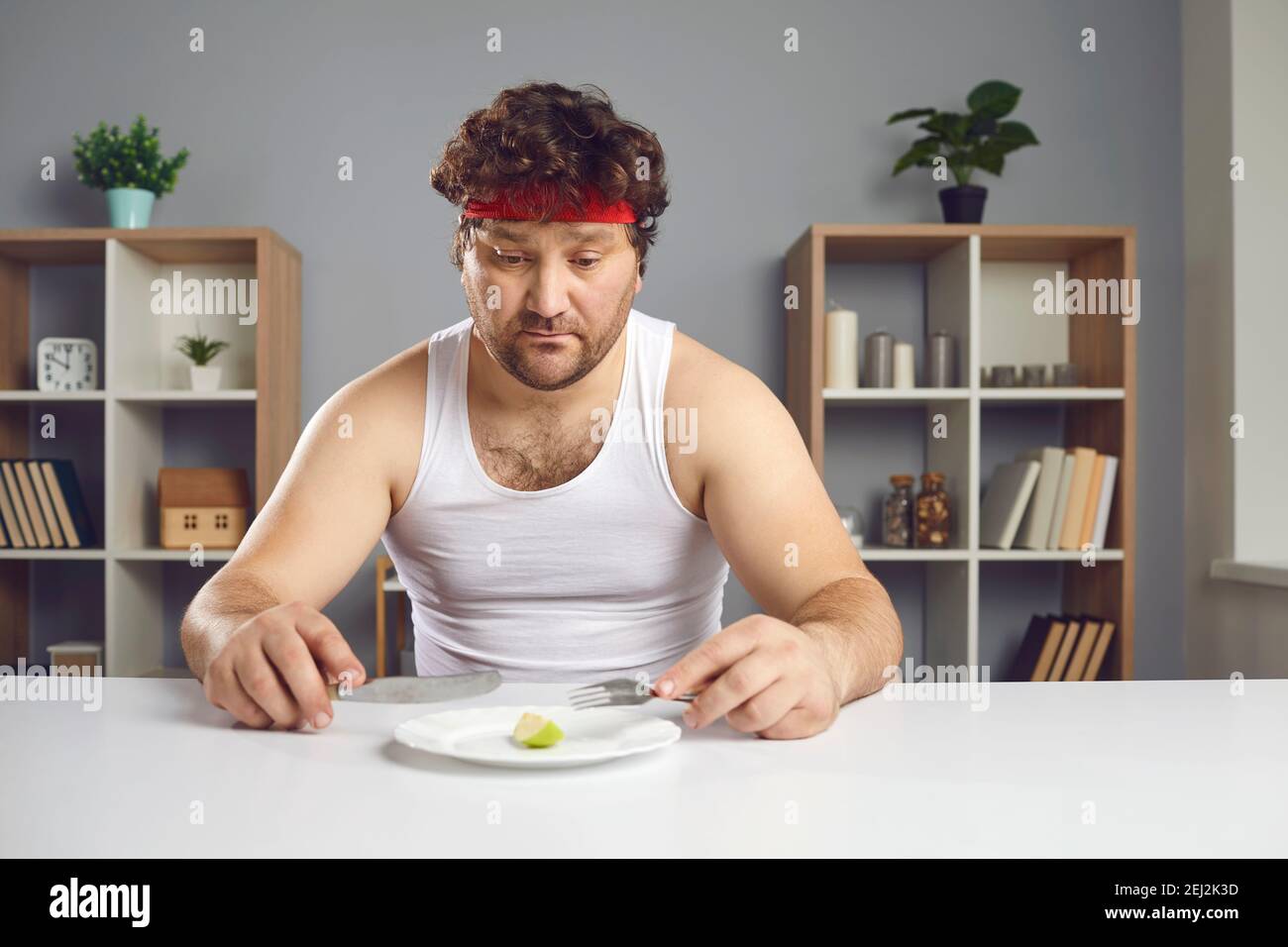Uomo triste su dieta rigorosa seduto a tavola e guardando a un piccolo pezzo di mela sul piatto Foto Stock