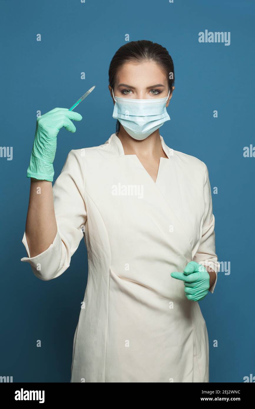 Medico o infermiere in maschera medica protettiva contenente siringa su sfondo blu, medicina, sicurezza e concetto di vaccinazione Foto Stock