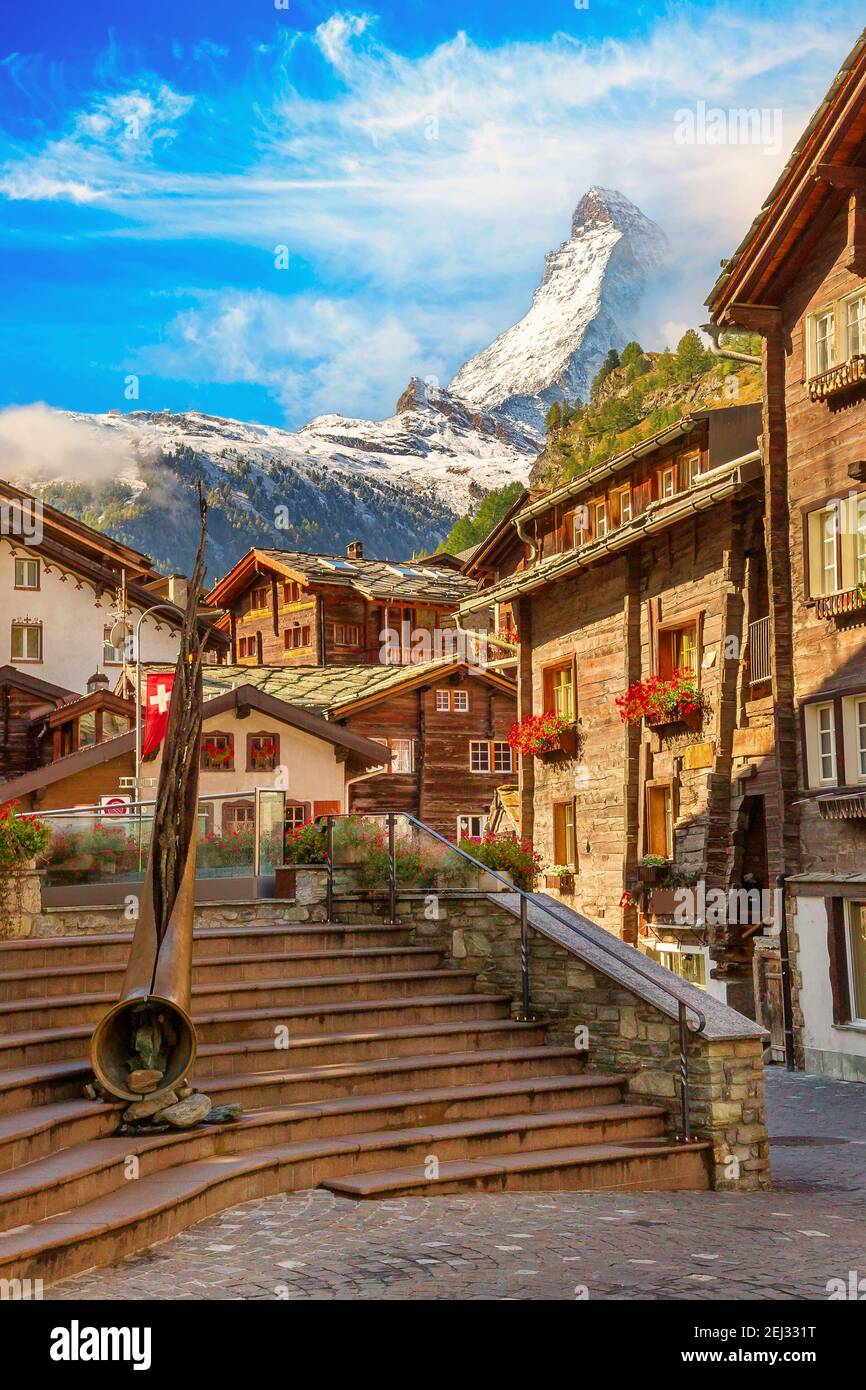 Zermatt, l'iconica vista sulla strada cittadina svizzera nella famosa località sciistica delle Alpi svizzere, il monte neve del Cervino, l'Alphorn in bronzo e le case Foto Stock