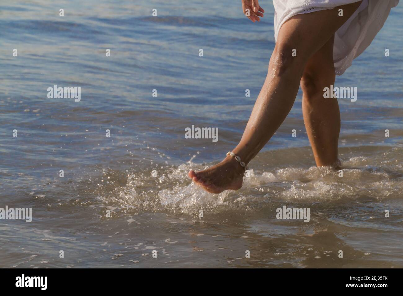 Un primo piano di piedi femminili con la caviglia che gioca acqua di mare Foto Stock