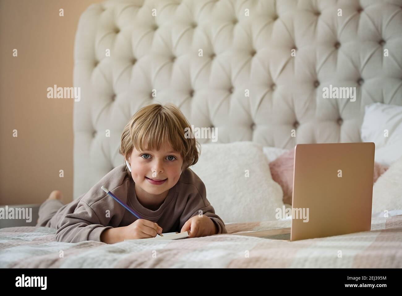 Bambino ragazzo carino che fa il lavoro che si trova sul letto a casa. Studiare online, imparare a distanza, autoeducazione Foto Stock