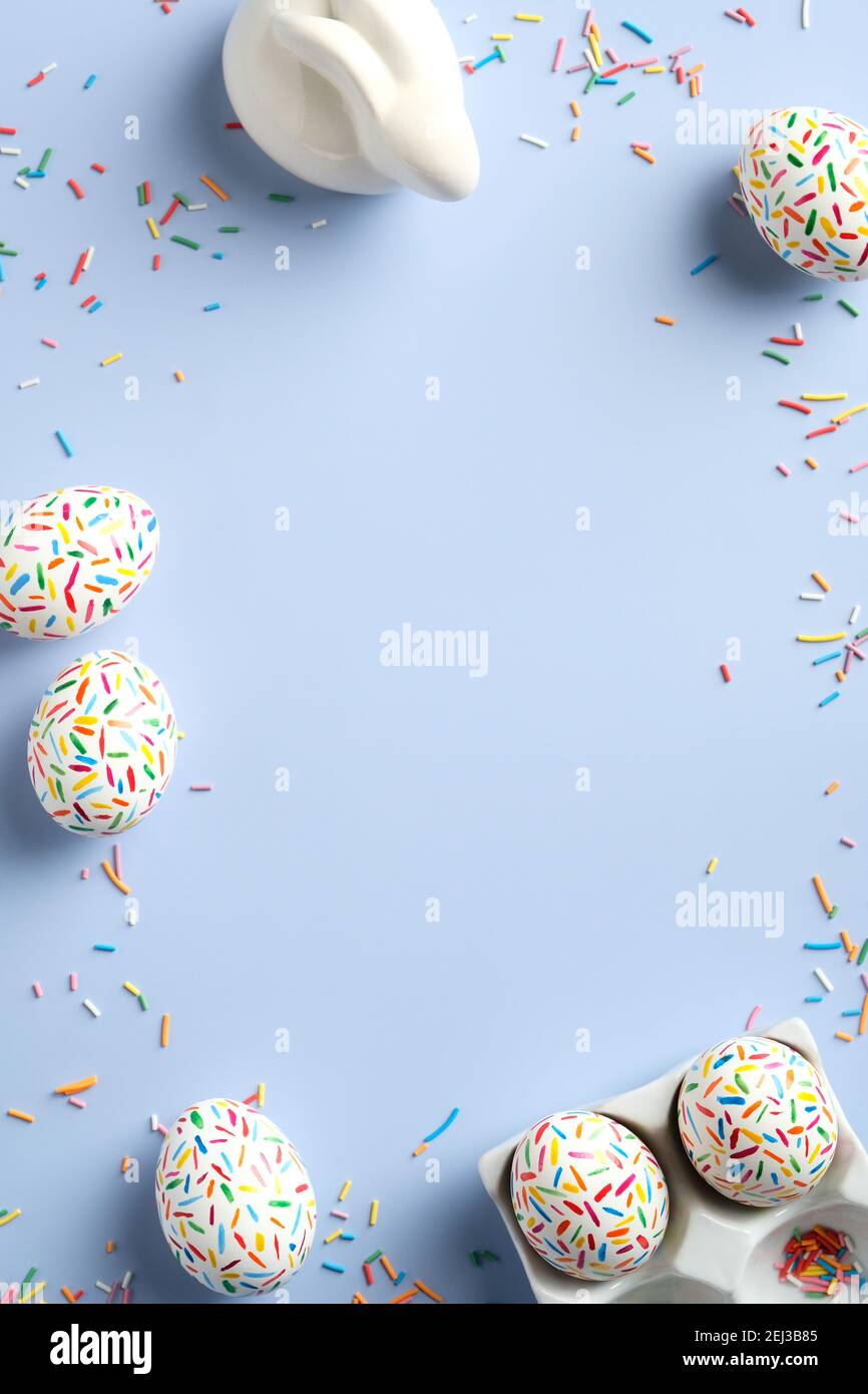 Cornice pasquale fatta di uova colorate coniglietto, dolci su sfondo blu pastello. Disposizione piatta, vista dall'alto, spazio per la copia. Buon disegno verticale del banner di Pasqua. Foto Stock