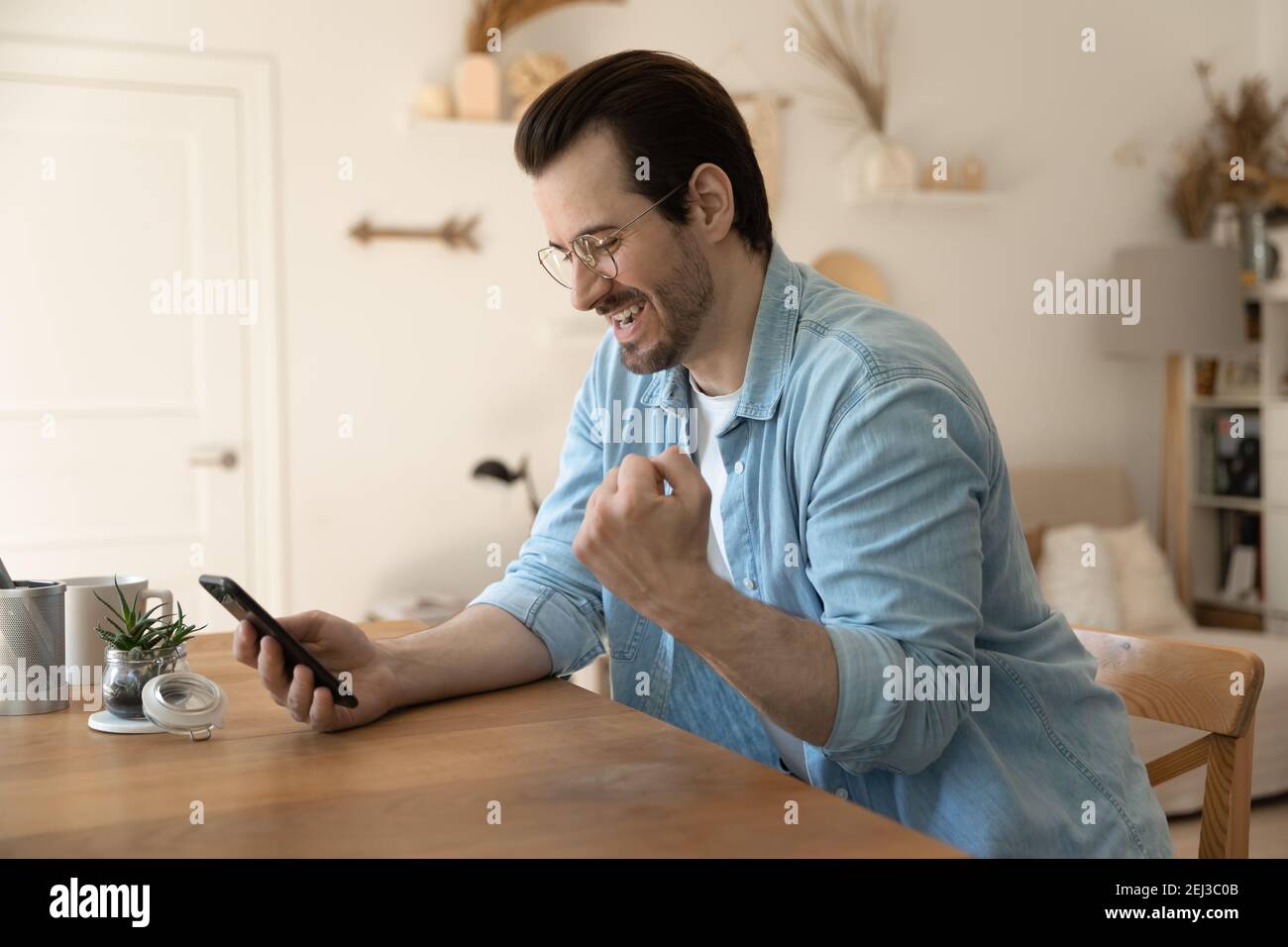 Un uomo millenario entusiasta festeggia la vittoria sullo smartphone Foto Stock