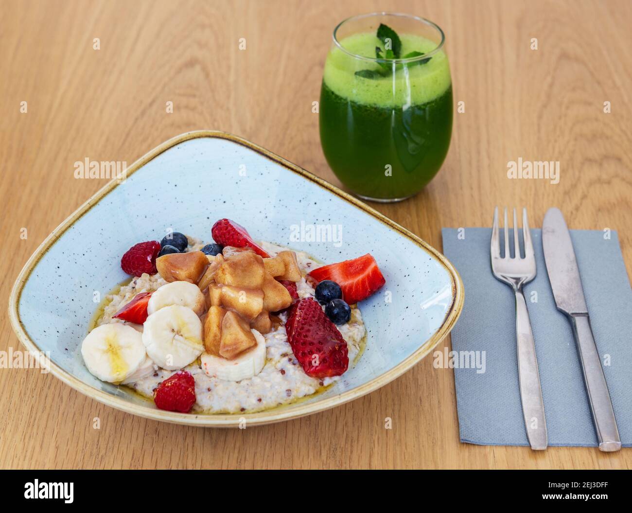 Ciotola di avena cotta con mela caramellata, banana e bacche ricoperte di miele. Succo di Kale da bere. Foto Stock