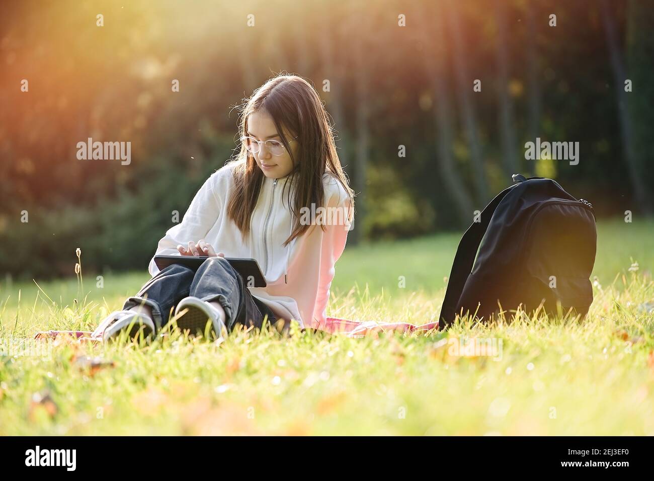 Cute adolescente ragazza è seduta sul parco in giornata di sole e utilizza tablet pc. Studenti e istruzione, giovani a scuola Foto Stock