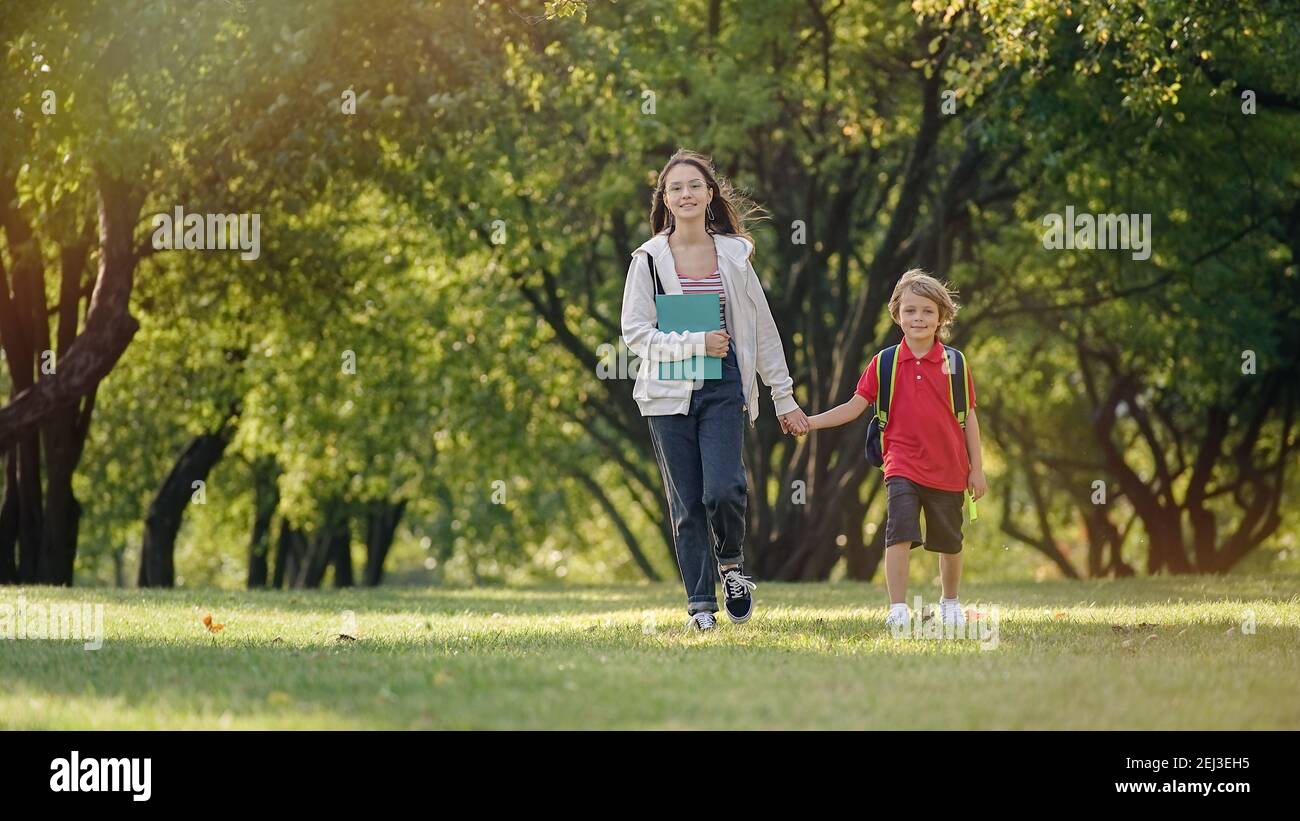 Scuola i bambini tornano dalla scuola di buon umore. Fratello e sorella camminano lungo il parco Foto Stock